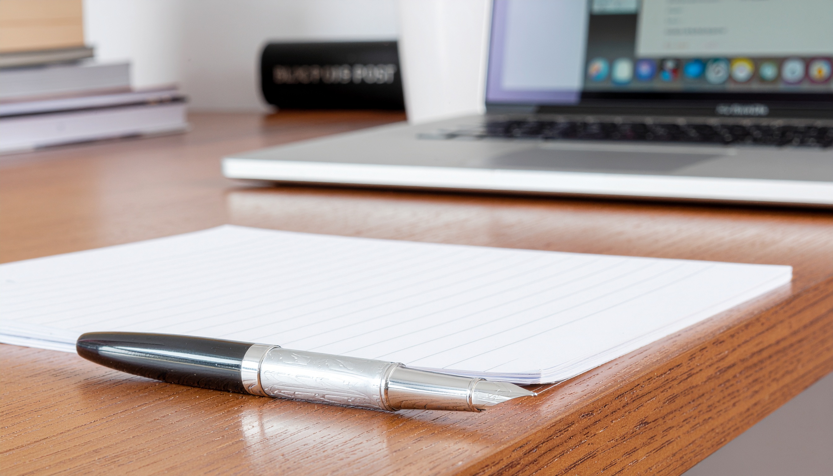 Notebook and pen on a desk beside a laptop